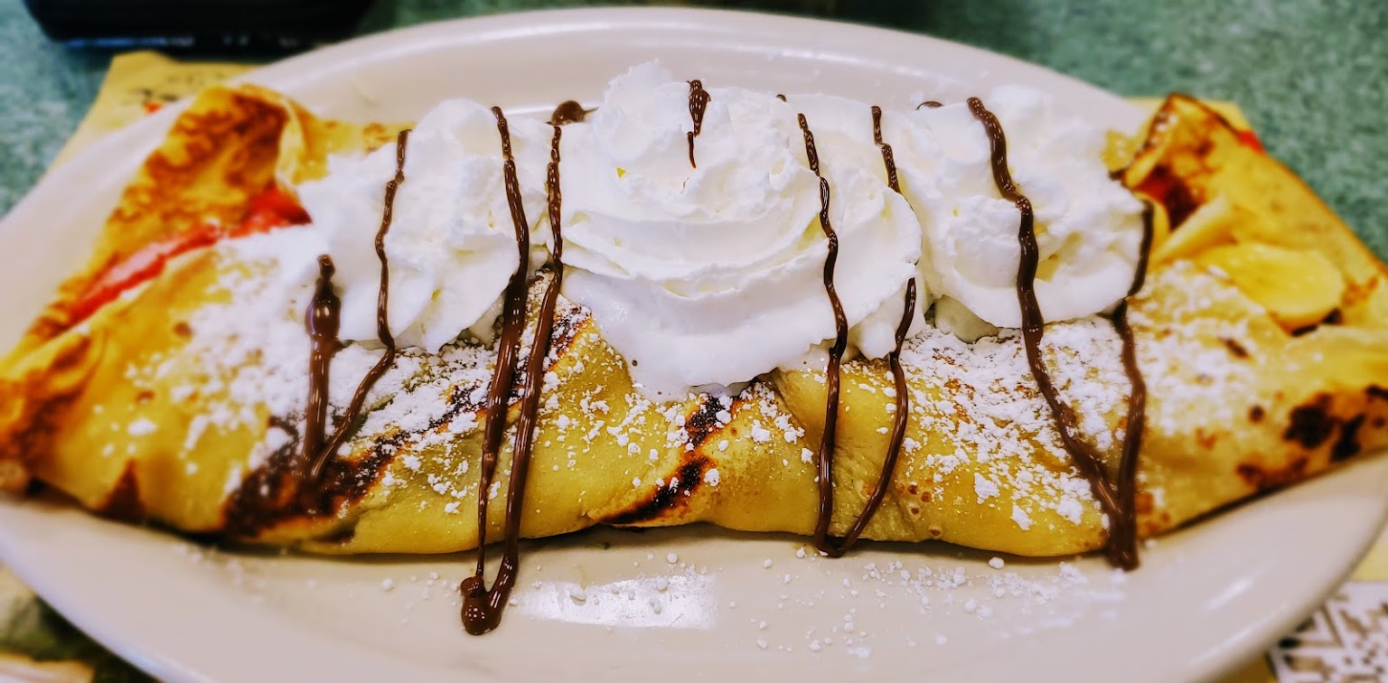 A sweet crepe filled with ripe strawberries topped with chocolate sauce and whipped cream.